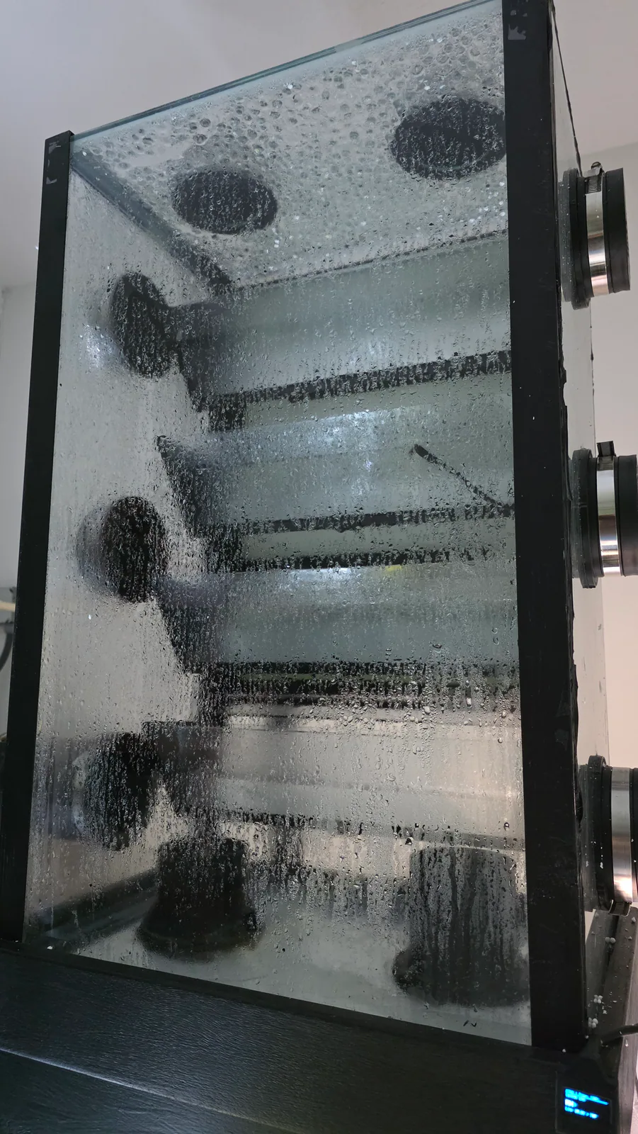 Misted glass chamber with horizontal shelves and circular side ports in the miniBIOTA rain system.